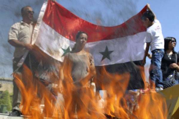 Manifestantes de partidos de esquerda segurar a bandeira síria enquanto queimam bandeiras americanas e israelenses em protesto contra possíveis ataques militares e para mostrar seu apoio ao regime do presidente da Síria, Bashar al-Assad, em frente à embaixada dos EUA em Amã  (MUHAMMAD HAMED)
