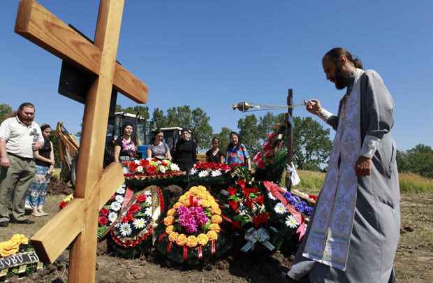 Padre realiza cerimônia fúnebre ao lado de conhecidos de Pyotr Ostapenko, 35 anos, uma das vítimam da inundação