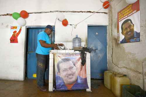 Morador de Caracas lava pratos em sua casa, entre cartazes com a foto do presidente Hugo Chávez: culto à personalidade do líder bolivariano