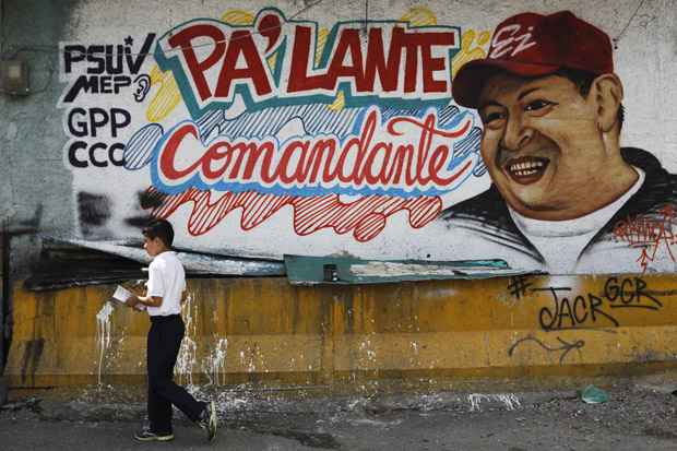 Criança caminha em frente a desenho do presidente em muro na Venezuela: Chávez permanece internado em estado estacionário, segundo médicos