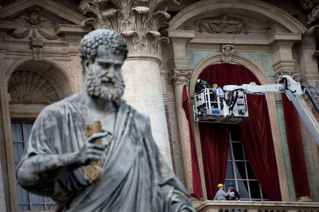 Trabalhadores penduram cortinas vermelhas na janela da basílica de São Pedro, onde o novo papa será apresentado depois do conclave