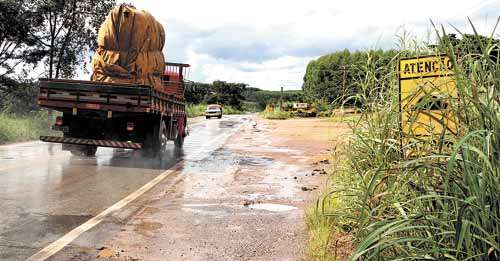 Caminhão trafega pela BR-080: intenso movimento de veículos grandes provoca falhas no asfalto, e mato alto encobre placas