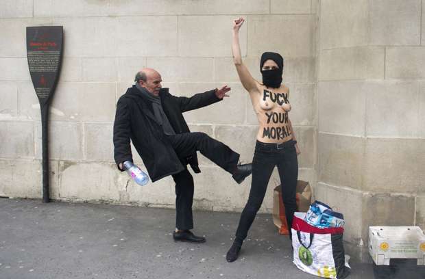 Homem chuta ativista ucraniana do movimento feminista Femen que faz topless. Ela levanta a mão em protesto contra islamitas em frente à Grande Mesquita de Paris