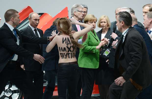 Manifestante de topless com mensagem nas costas caminha para o presidente russo, Vladimir Putin (E), e a chanceler alemã, Angela Merkel (C) durante a sua visita a Hanover, na Alemanha