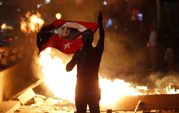 Manifestante com bandeira na mão faz gestos: protesto dura vários dias