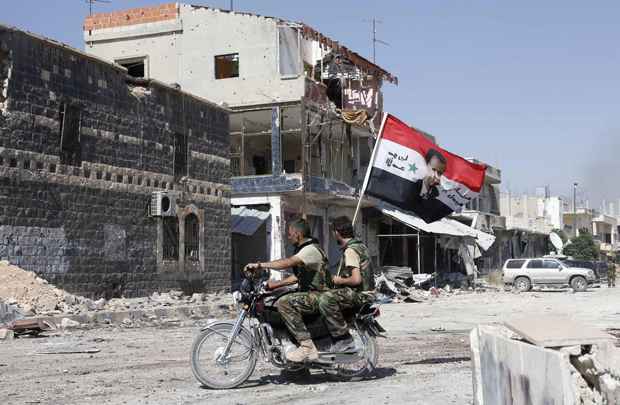 Forças leais ao presidente da Síria, Bashar al-Assad carregam bandeira nacional em moto em Qusair, depois que o exército sírio tomou o controle de rebeldes