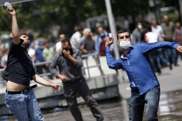 As pessoas jogam pedras contra canhões de água durante um protesto na praça Kizilay no centro de Ancara.