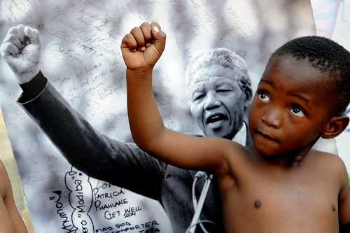 Um jovem membro da Trupe Cultural Maitibolo posa em frente a uma fotografia do ex-presidente sul-africano Nelson Mandela