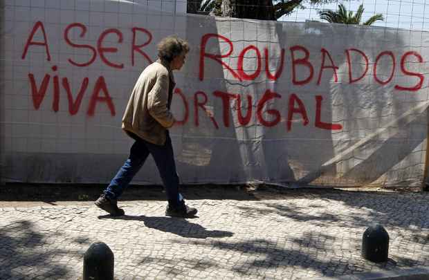 Homem caminha por rua de Lisboa onde foi colocada uma faixa contra a crise econômica que atingiu no país