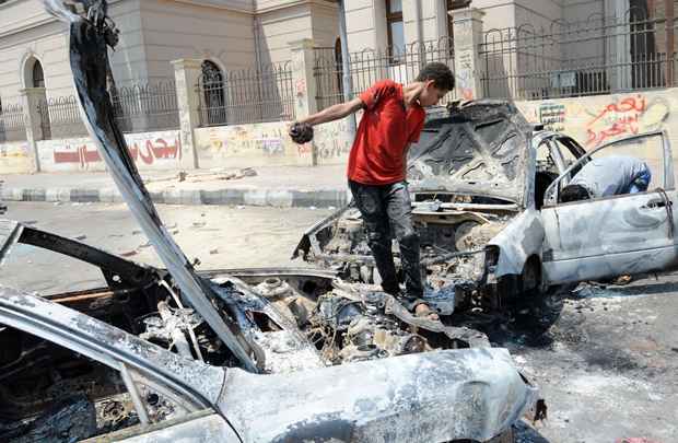 Jovem egípcio inspeciona um carro queimado perto da Universidade do Cairo