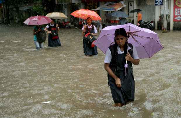 Estudantes indianos atravessam rua inundada durante pancadas de chuva em Mumbai