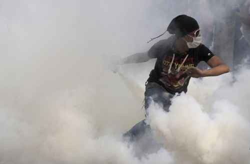 Manifestante anti-Mursi corre para lançar lata de gás lacrimogêneo para trás durante confrontos com a polícia na praça Tahrir, no Cairo