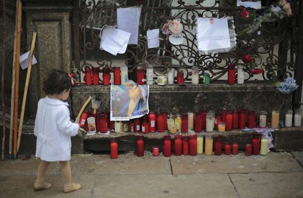 Criança passa por velas velas e flores deixadas do lado de fora de uma catedral em memória das vítimas do acidente de trem em Santiago de Compostela, no noroeste da Espanha