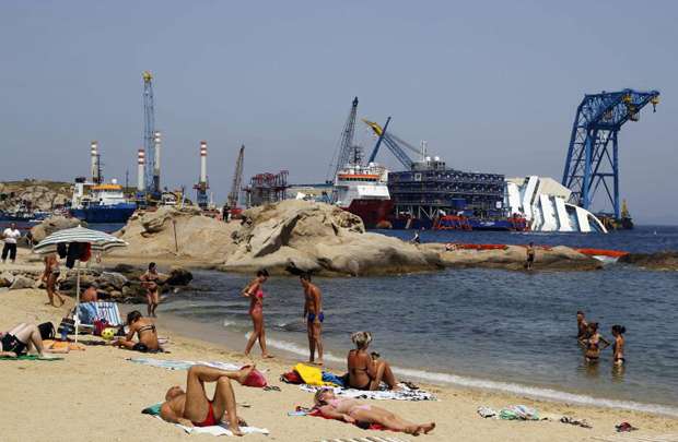 Pessoas tomam banho em frente de ao navio Costa Concordia, que naufragou em janeiro de 2012