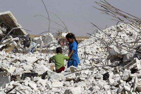 Menina ajuda o irmão fazer o seu caminho entre os escombros de uma casa danificada em zona rural da Syria