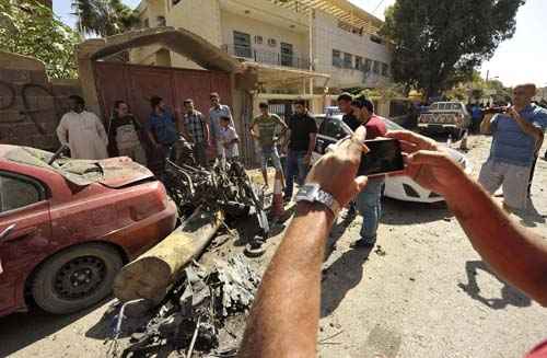 Pessoas tiram fotos dos destroços de um carro depois que explodiu do lado de fora do consulado sueco em Benghazi