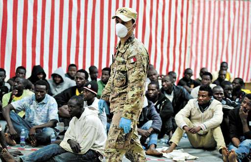 Soldado caminha diante de imigrantes africanos socorridos perto da Ilha de Lampedusa: vigilância na Sicília