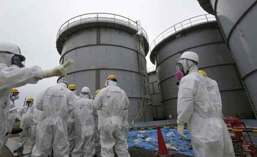 Jornalistas vestem roupas de proteção e máscaras de pé em frente a tanques de armazenamento de água radioativa na área onde a água radioativa vazou de um tanque de armazenamento, em Fukushima