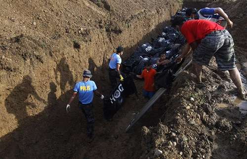 Voluntários e policiais carregam sacos para corpos de uma vala comum para o enterro no rescaldo de super tufão Haiyan na cidade de Tacloban