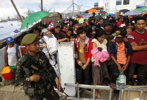 Um soldado monta guarda em frente a uma multidão que aguardava no portão do aeroporto de Tacloban