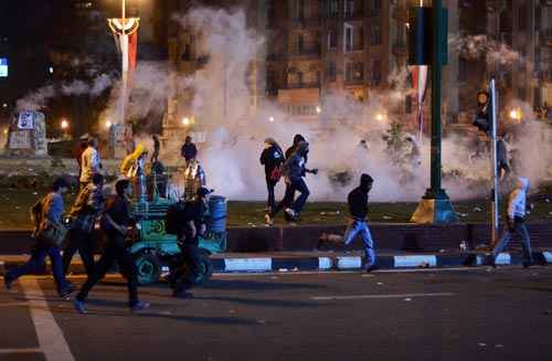 Manifestantes anti-militares egípcios correm para se esconder do gás lacrimogêneo lançado pela polícia durante confrontos na praça Tahrir, no Cairo