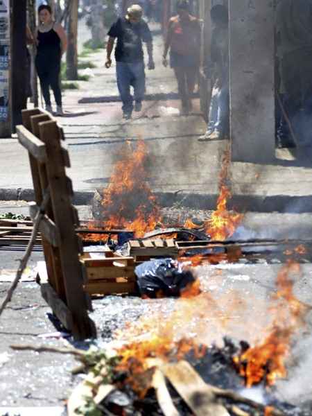 Pessoas andam atrás de uma barricada criada para desencorajar os saqueadores e ladrões durante a greve da polícia, em Córdoba