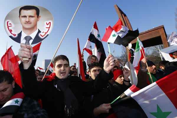 Partidários do presidente sírio, Bashar Al-Assad, carregam fazem ato em frente à sede europeia das Nações Unidas, em Genebra