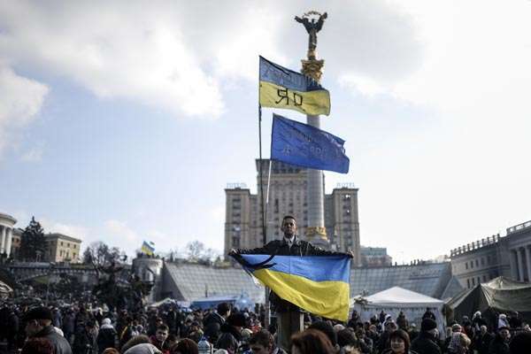 Homem segura bandeira ucraniana em ato na Praça da Independência, em Kiev