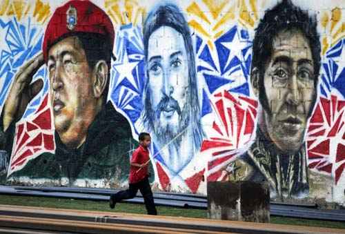 Venezuelanos fazem pintura mural com retrato do ex-presidente venezuelano, Hugo Chávez, Jesuschrist e o herói da independência Simon Bolívar