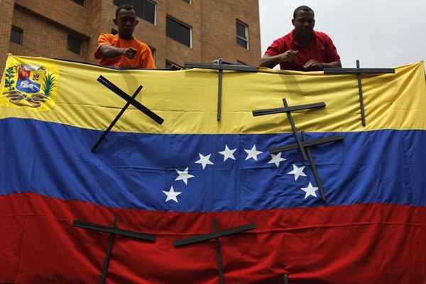 Trabalhadores removem cruzes de madeira em uma bandeira, colocadas para lembrar as vítimas da violência depois de um protesto contra o governo do presidente da Venezuela. De acordo com o Sindicato Nacional de Trabalhadores da Imprensa, pelo menos 89 jornalistas foram agredidos, roubados, ou detidos sem justificativa desde o início dos protestos que cruzam o país há um mês