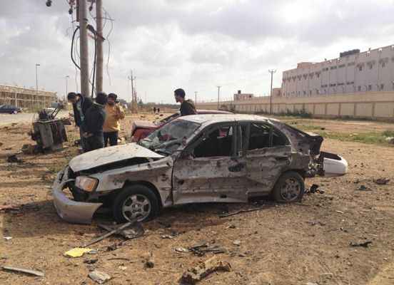 Homens param ao lado de um carro danificado após explosão na cidade oriental de Benghazi