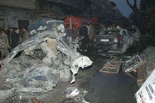 Pessoas se reúnem em torno de destroços depois da explosão de um carro-bomba no bairro al-Zahra'a na cidade de Homs