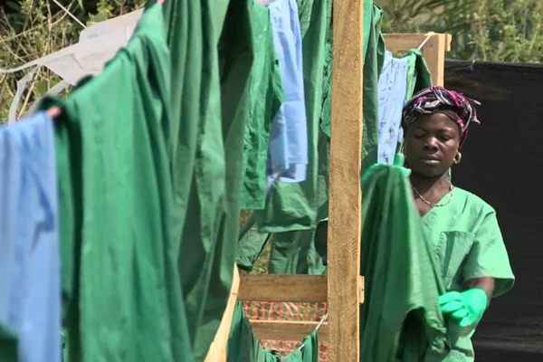 Mulher do grupo humanitário Médicos Sem Fronteiras seca equipamentos de proteção após lavagem em acampamento médico no sul da cidade de Gueckedou, Guiné