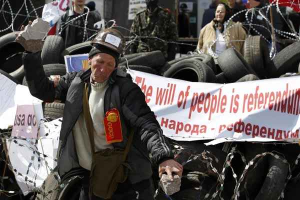 Manifestante pró-Rússia quebra pedaço de pedra em barricada diante de prédio do governo regional em Donetsk, na Ucrânia