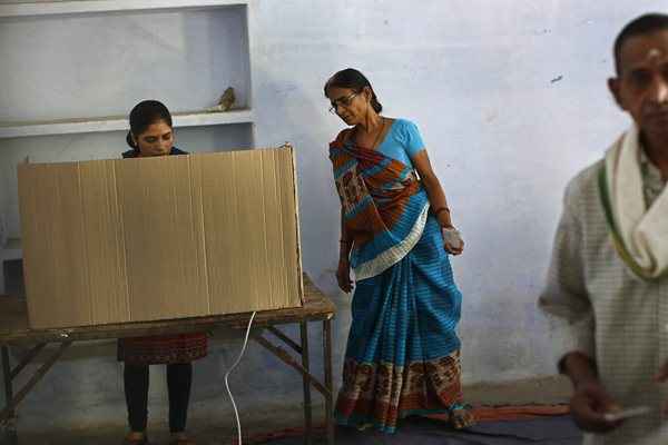 Uma mulher observa enquanto outra lança seu voto numa assembleia de voto na fase final das eleições gerais em Varanasi, Índia