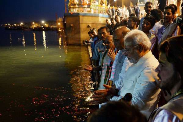 O líder hindu acendeu uma lâmpada a óleo e se sentou no centro de um tablado com flores às margens do Ganges, rio purificador para os hinduístas