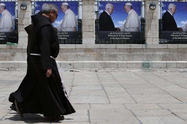 Padres franciscanos passam banners com retratos de papa Francisco e o presidente palestino Mahmud Abbas, perto da Igreja da Natividade, em Belém, na Cisjordânia