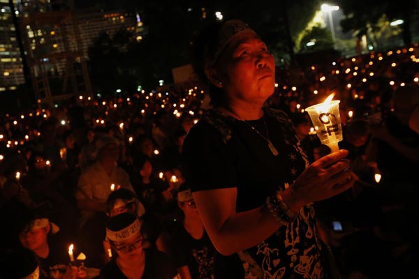 Pessoas carregam velas em homenagens às vítimas do massacre, em Hong Kong