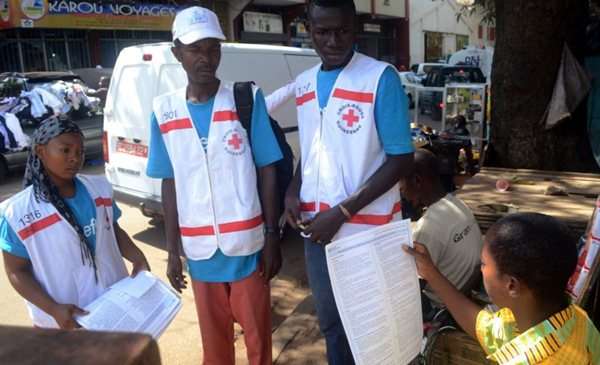 Membros da Cruz Vermelha do Guiné falam com um morador durante uma campanha de sensibilização sobre o vírus Ebola