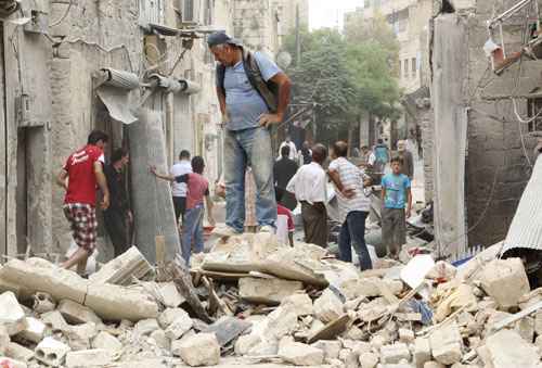 Pessoas obsrvam local atingido por bomba, supostamente jogada por forças leais ao presidente reeleito Bashar Al-Assad, no distrito de Qadi Askar, em Aleppo