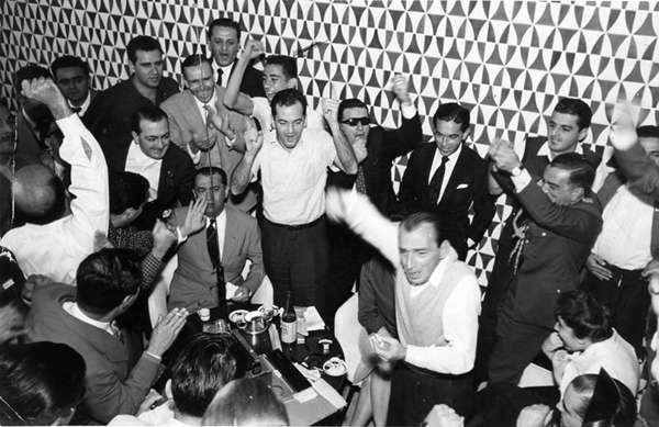 Juscelino ouve a transmissão do jogo no Brasília Palace Hotel ao lado da família, de auxiliares e de jornalistas. Um deles, Paulo Manhães, veio, foi fotografado e ficou. Na foto, Márcia Kubitschek com a mão na boca