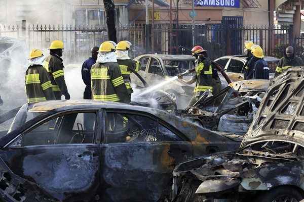 Bombeiros apagam fogo de carros após explosão de uma bomba em uma área comercial lotada em Abuja. A explosão destruiu o popular centro comercial Plaza Banex