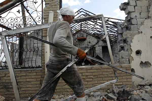 Homem remove os restos de edifício em ruínas, na periferia da cidade ucraniana de Slaviansk