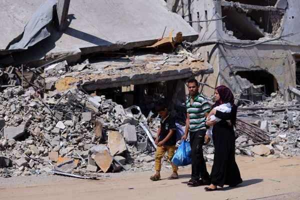 Uma família palestina passa por edifícios destruídos em sua vizinhança, no norte da Faixa de Gaza