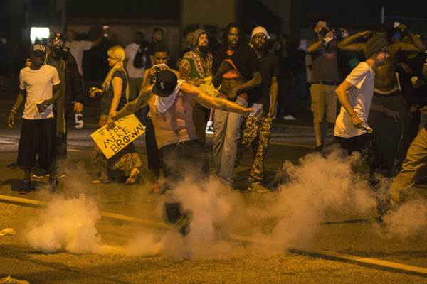 Manifestante chuta bomba de gás lacrimogêneo para a polícia em protesto pelo assassinato de jovem negro, em Ferguson, no Missouri