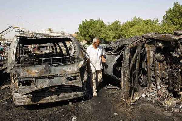 Homem olha destroços de carros após três explosões em bairro xiita de Bagdá