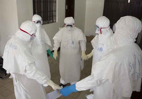 Profissionais de saúde de mãos dadas antes de entrar em centro de tratamento do ebola na Clínica Ilha, em Monróvi