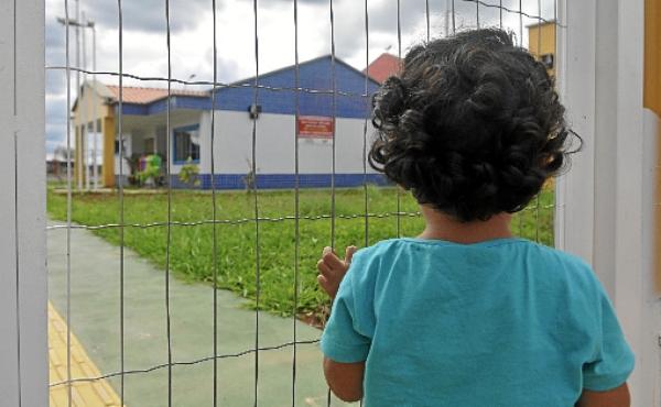 Pelo portão, criança observa uma creche fechada em Samambaia