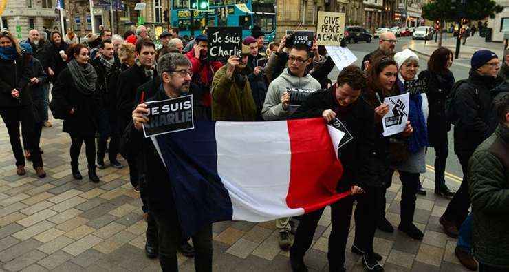 Em Liverpool, na Inglaterra, grupo faz manifestação com bandeira francesa e cartazes: 