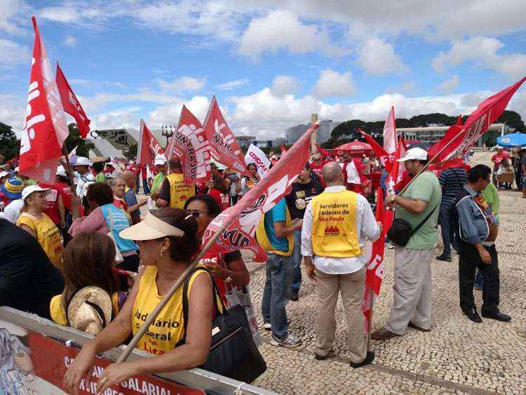 Grupo de trabalhadores está reunido em frente ao Planalto, com faixas, bandeiras e cartazes